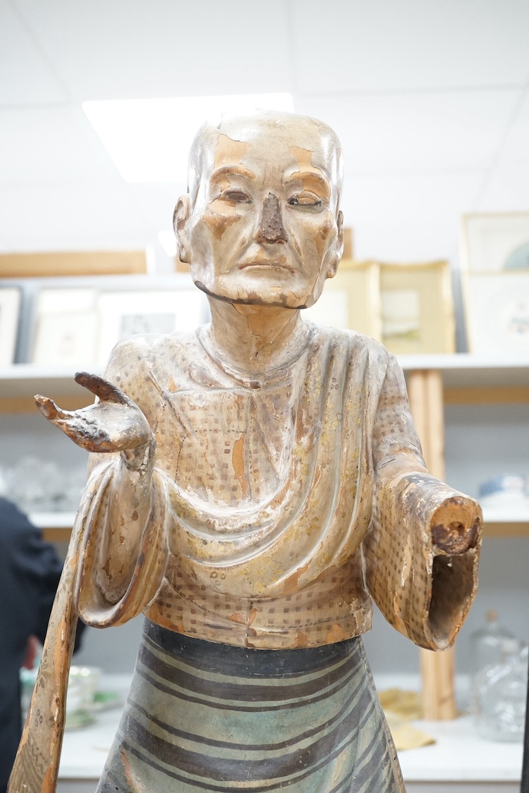 A pair of large Indonesian carved and painted wood figures of an old monk and a lady wearing a sarong, 19th/early 20th century, 70cm. Condition - hand on monk figure broken.